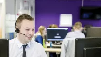 Man smiling at his desk, wearing a headset