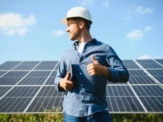 Man standing in front of free-field solar power plant, thumbs up.