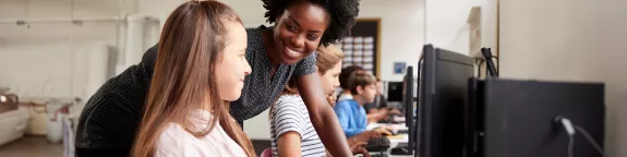 Image of a teacher with a student who is on a computer at school. 