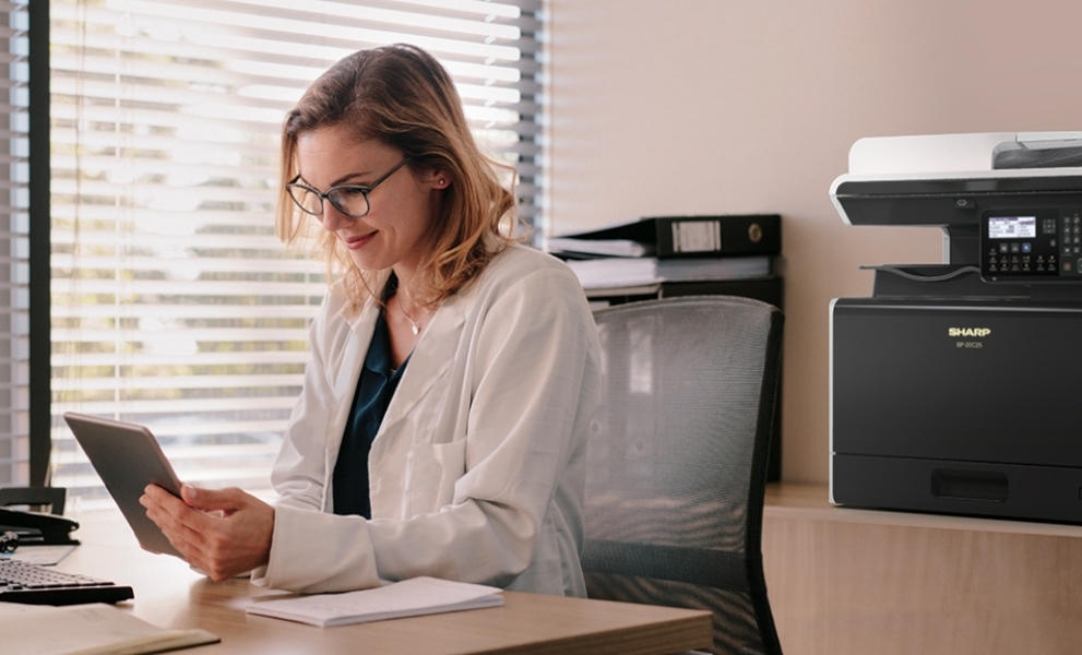 Woman at desk in small office with printer in background