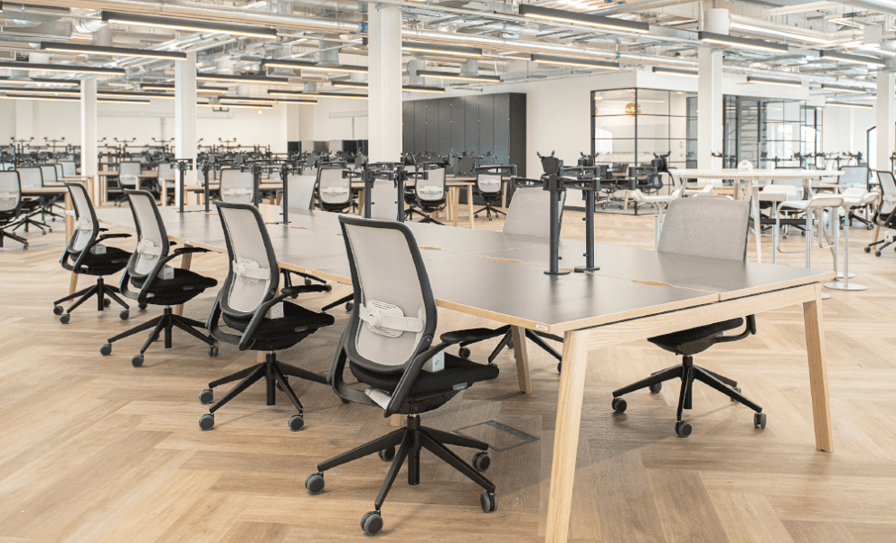 Open plan office environment with wooden flooring and wooden bench desking with task chairs